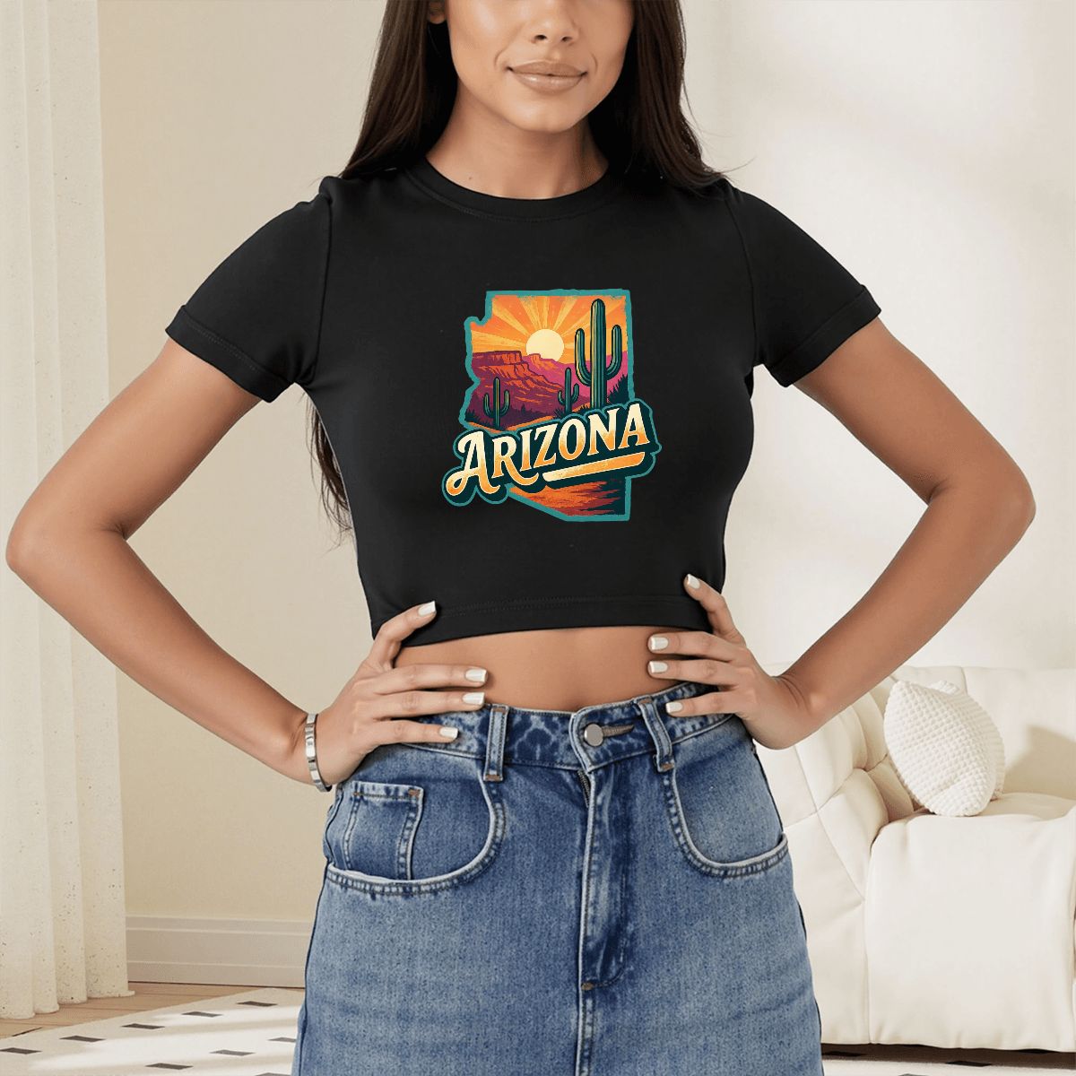 A woman wearing a black cropped t-shirt with a colorful 'Arizona' desert landscape graphic on the front, paired with a blue denim skirt in a brightly lit indoor setting.