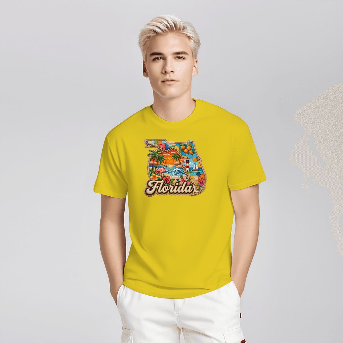 A young man with blonde hair wearing a bright yellow t-shirt with a colorful graphic of the state of Florida filled with tropical scenery and the word 'Florida' written in script. He is also wearing white pants, standing against a light gray studio background.