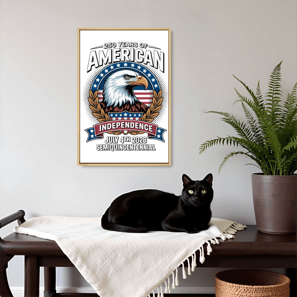 A framed vertical poster with a patriotic eagle design and the text '300 Years of American Independence July 4th 2025 Semi-Quarterly' is displayed on a light gray wall above a dark wooden bench with a black cat resting on a white throw blanket, next to a potted green plant.